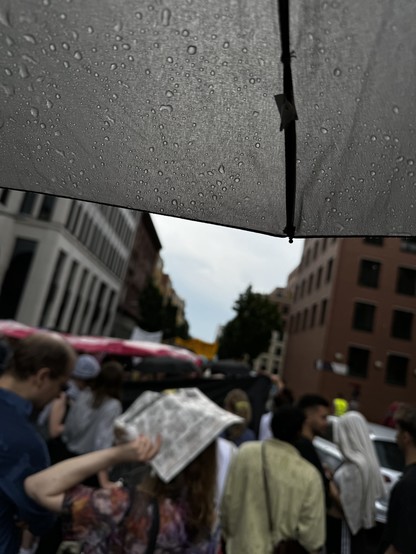 Foto einer Demo gegen Mietenwahnsinn. Es regnet. Das Foto ist von unter einem Regenschirm gemacht.