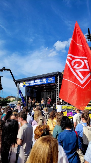 Rote Fahne der IGM vor einer Bühne vor der eine große Menschenmenge steht