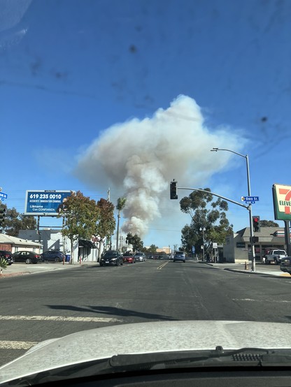 Blue sky with a big plume of smoke in the distance. A street light is red in the foreground.